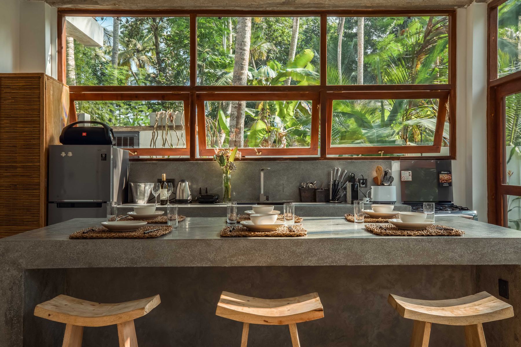 Concrete kitchen counter with wooden stools in front of large windows onto the garden