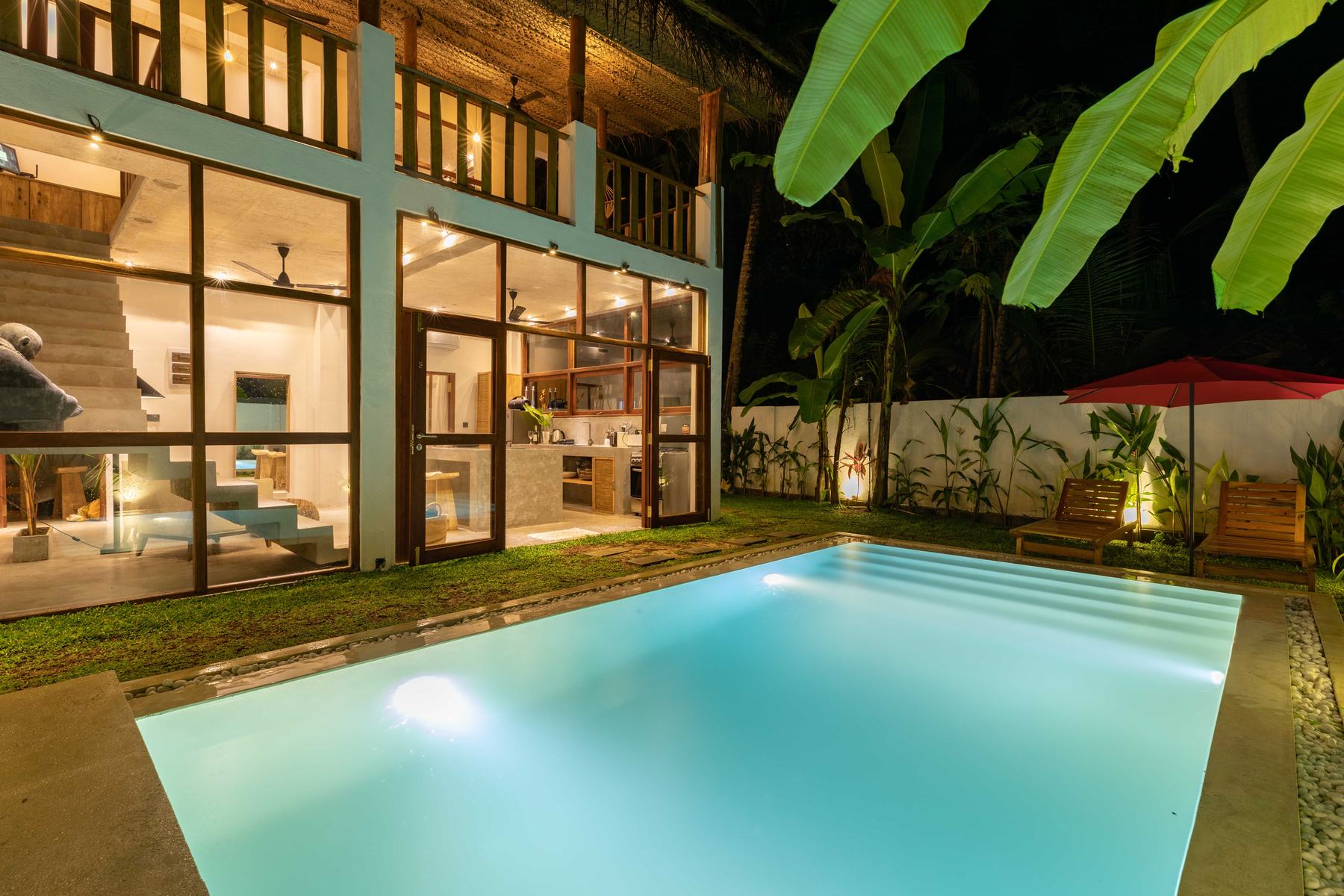 The pool lit up at night with the glass-fronted house glowing behind it